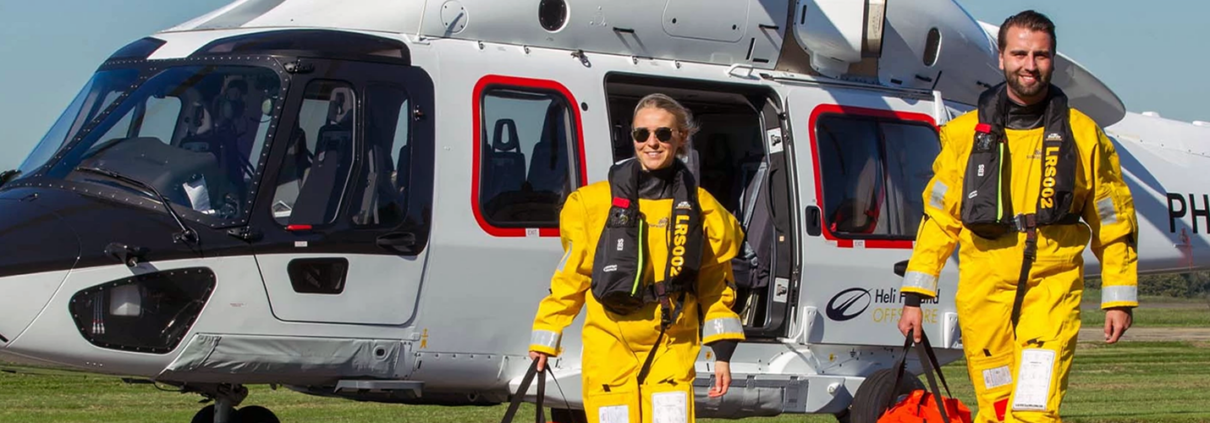 Man en vrouw van bedrijf Biardo Survival Suits stappen uit helicopter in geel pak.